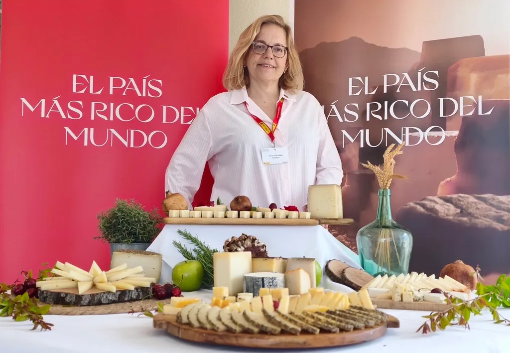 Ruth Lozano standing behind a table laid with a large selection of Spanish cheeses cut into wedges and cubes, at an agrifood promotion event.